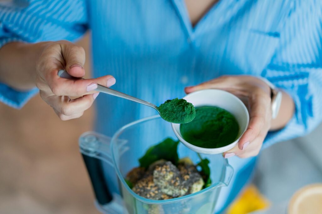 Close up woman adding spirulina green powder during making a smoothie in the kitchen. Superfood
